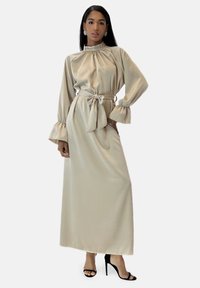 Langærmet, taupefarvet satin-kjole med høj hals og flæseærmer, indsnøret i taljen med et matchende bælte og med gulvlængde design.