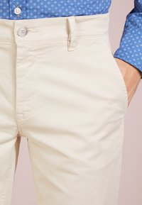 Beiga bomullbyxor med rak passform, med knäppning fram, bälteshällor och sidfickor. Slät textur.