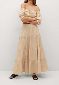 Top de tirantes con los hombros al descubierto en color beige, combinado con una falda de largas capas hasta los tobillos. Tejido suave con un ligero brillo, acompañado de sandalias de tiras negras.