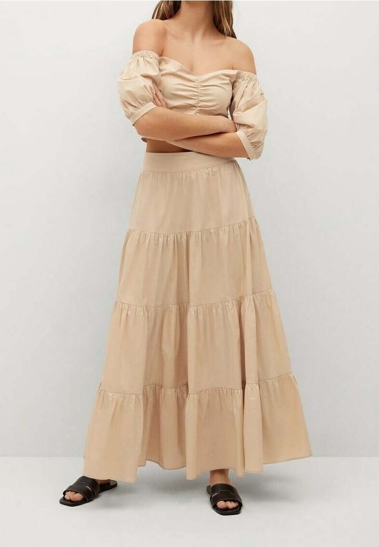 Top de tirantes con los hombros al descubierto en color beige, combinado con una falda de largas capas hasta los tobillos. Tejido suave con un ligero brillo, acompañado de sandalias de tiras negras.