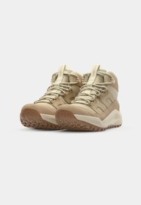 Beige Wanderschuhe mit robustem Design, ausgestattet mit einer strukturierten Gummisohle, verstärkter Zehenkappe und einem Schnürverschluss mit gepolstertem Kragen.
