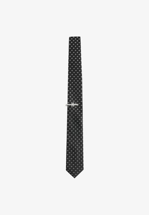 Black silk tie with a repeated small white floral pattern, featuring a silver tie clip for secure fastening. Tapered end, smooth texture.