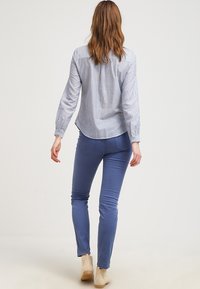 Chemise rayée bleu clair à manches longues, associée à un jean slim bleu et des bottines beige à la cheville, vue de dos.