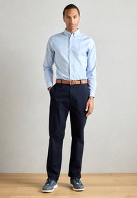 Hellblaues Button-up-Shirt, marineblaue Hose, brauer Gürtel und graue Turnschuhe. Formschlüssiges Design mit langen Ärmeln und einem einfachen Kragen.