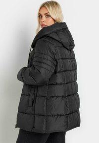 Svart puffjacka med huva, med horisontella quiltade sektioner, sidfickor och ett framfäste med dragkedja. Texturerad yta.