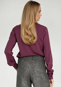Długa rękaw, ciemnofioletowa bluzka o gładkiej fakturze, w połączeniu z wysokimi, szarymi spodniami o teksturowanej powierzchni i elastycznym paskiem.