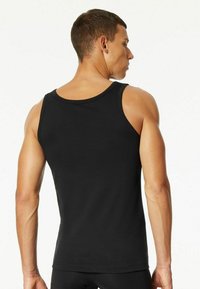 Black tank top made of cotton, featuring a round neckline and wide shoulder straps, fitted cut, and smooth texture.