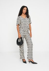 Combinaison imprimée avec un décolleté en V, des manches courtes et une taille cintrée. Le motif présente des gouttes d'eau bleu marine sur un fond crème. Accessoirisée avec un sac noir.