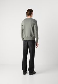 Lichtgroene trui met een ronde hals en geribbelde manchetten, gecombineerd met zwarte, relaxed-fit jeans en zwarte schoenen. Textuur van de stof zichtbaar.