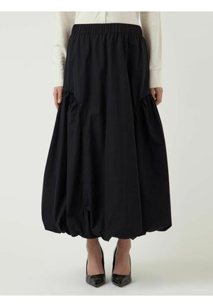 Jupe midi noire à ourlet ballon avec des détails froncés sur les côtés, portée avec des talons pointus noirs et un top blanc.