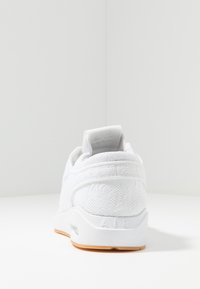 Vit sneaker med en texturerad övre del av tyg, en dämpad häl och en gummiyttersula. Har "AIR"-logotyp på baksidan. Enkel design.