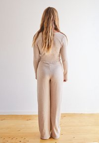 Completo a due pezzi in maglia a coste beige con top aderente e pantaloni a gamba larga. Presenta un orlo ondulato sul top e un tessuto testurizzato.