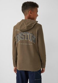 Olivgrüner Hoodie mit großem weißen "BOSTON"-Druck und dunklen Akzenten, strukturiertem Stoff, langen Ärmeln und einer Rückentasche.