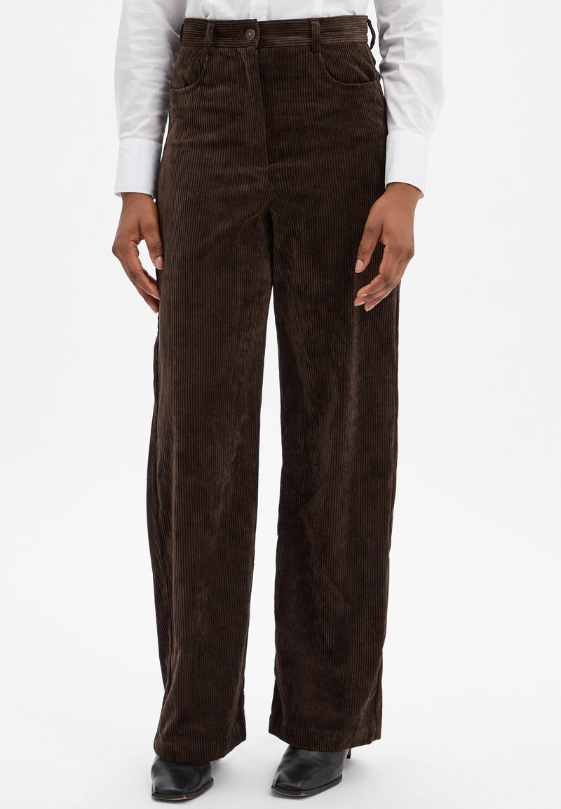 Brązowe szerokie spodnie z korduroju o pionowej fakturze, z przednimi kieszeniami i wysokim stanem, w połączeniu z czarnymi butami na cienkim obcasie.