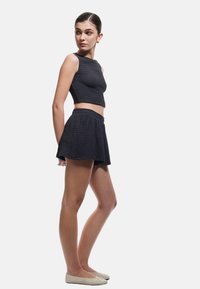 Conjunto de dos piezas oscuro y texturizado que incluye un top corto y shorts acampanados, ambos con una cinturilla elástica, complementado con unas bailarinas de color claro.