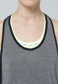 Canottiera atletica grigia con scollatura rotonda, rifinita in nero e sovrapposta a una maglietta intima atletica gialla chiara con un design a motivo.