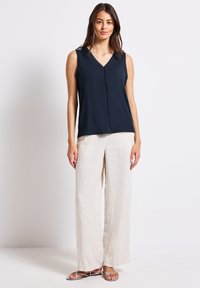 Top senza maniche di colore blu navy con scollatura a V, caratterizzato da una cucitura decorativa centrale; abbinato a pantaloni larghi in lino di un leggero colore beige.