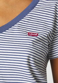 Modrá a bílá pruhovaná trička s výstřihem do V, vyrobené z měkké bavlny, s malým červeným vyšitým logem Levi's na přední straně.