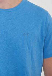 Maglietta blu a maniche corte in morbido cotone, con colletto a coste e un piccolo logo triangolare ricamato sul lato sinistro del petto.