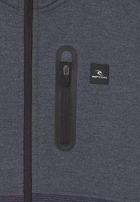 Herre zip-up hoodie i mørkeblå stof med en lynlås brystlomme med en sort lynlås og et Rip Curl-logo på fronten.