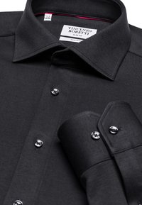 Camicia nera slim-fit con colletto strutturato, caratterizzata da una texture liscia, bottoni metallici e accenti rossi a contrasto all'interno del colletto.