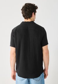 Camisa negra de manga corta con un patrón texturizado, que presenta un cuello puntiagudo y un dobladillo recto. Llevada con jeans de mezclilla azul claro.