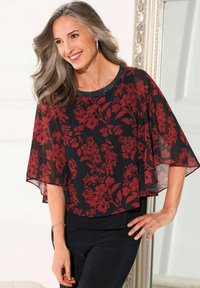 Blusa nera trasparente con motivo floreale rosso, maniche corte a campana e scollatura rotonda con dettagli in perline. Indossata sopra pantaloni neri.