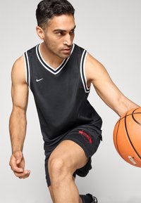 Svart basketballtrøye med hvite detaljer og v-hals; kombinert med svarte shorts med rødt "BULLS"-logo. Spiller som dribler en basketball.
