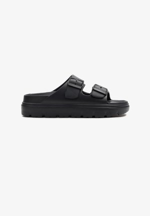 Sandalia negra tipo slip-on con suela gruesa y dos tiras ajustables con hebilla, diseñada para uso casual.