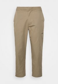 Béžové zkrácené kalhoty z hladké látky s plochým pasem a malým černým logem na levé kapse.