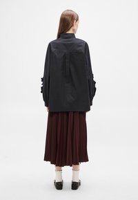 Črna prevelika srajca z visokim ovratnikom in nabranimi rokavi, kombinirana z gubano temno rdečo krilo. Dodatki vključujejo bele nogavice in črne čevlje.