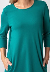 Turquoise langemouw top met een ronde halslijn, zachte textuur en zijzakken. Heeft een relaxte pasvorm en subtiele naaddetails.