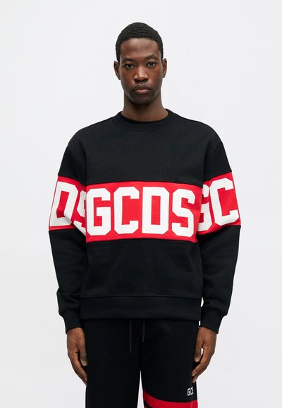 Μαύρο φούτερ με μια κόκκινη και λευκή οριζόντια λωρίδα που περιλαμβάνει μεγάλα γράμματα. Φτιαγμένο από μαλακό ύφασμα, με στρογγυλή λαιμόκοψη και ριμπ μανσέτες.