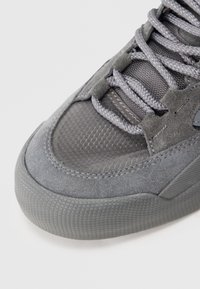Close-up van de textuur van de teen van een grijze sneaker, met suède overlays, een bovenwerk van mesh en strak aangetrokken bijpassende grijze veters.