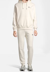 Kremowa bluza z kapturem z przednią kieszenią i sznurkami, w zestawie z pasującymi spodniami dresowymi ozdobionymi małym logo i elastycznymi mankietami.