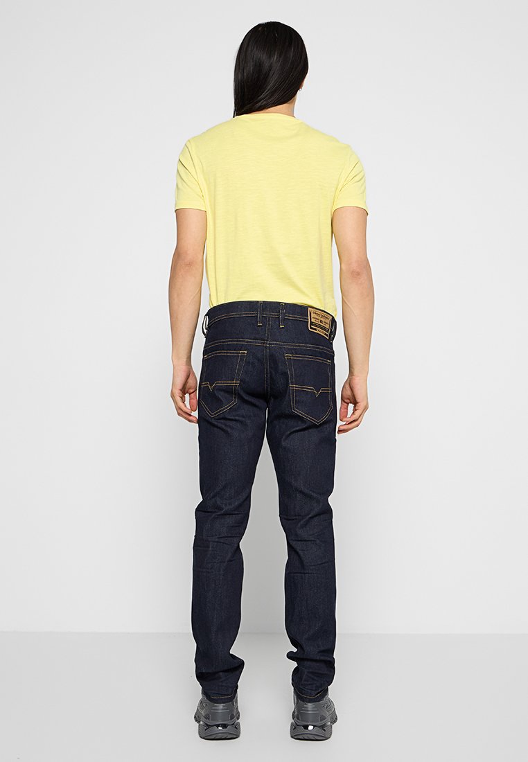 Gelbes Kurzarm-T-Shirt, kombiniert mit dunkelblauen Jeans. Die Jeans haben ein klassisches Fünf-Taschen-Design und sichtbare Nähte.