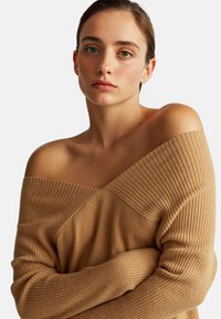 Maglione beige off-the-shoulder caratterizzato da una texture a coste verticali e un motivo a maglia diagonale sul davanti, con una vestibilità morbida.
