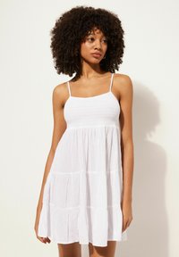 Weißes, ärmelloses Kleid mit einem gerüschten Oberteil und einem gestuften Rock. Hergestellt aus leichtem Stoff mit einer weichen Textur. Dünne, verstellbare Träger.