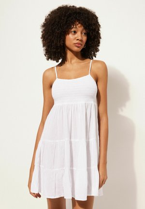 White, sleeveless dress with a smocked bodice and tiered skirt. Made from lightweight fabric with a soft texture. Thin adjustable straps.