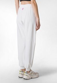 Witte, loszittende broek met elastische boorden en tailleband. Heeft een klein roze label en een gladde textuur. Gemaakt in combinatie met lichtgekleurde sneakers.