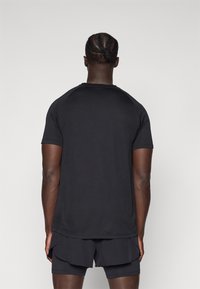 T-shirt de sport noir avec une texture lisse, des manches courtes et un col rond. Porté avec un short assorti de couleur sombre.