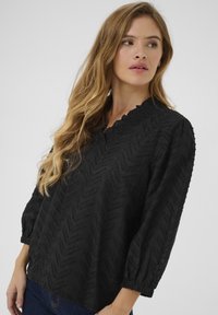 Mustarblouse, mille tekstuuriga chevron mustriga, ruffle-dekolteega ja 3/4 puffvarrukatega, valmistatud kergest kangast.