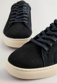 Schwarze Wildledersneaker mit glatter Oberfläche, runder Spitze und cremefarbener Gummisohle. Ausgestattet mit dunkler Schnürung und strukturierten Akzenten an der Sohle.