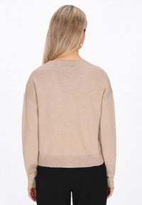 Beiger Pullover mit lockerer Passform, geripptem Saum und langen Ärmeln. Aus einem weichen, strukturierten Material gefertigt. Sichtbare Nähte entlang der Säume.