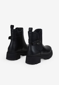 Botas de cuero negras hasta el tobillo con cremallera lateral, una correa decorativa con hebilla y una suela de goma gruesa con relieve.