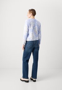 Lyseblå blomstermønstret strikkegenser med rund hals, ribbestrikkede mansjetter og hem. Kombinert med mørkeblå rette jeans og beige platåsko.