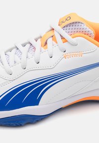 Bílé sportovní boty s modro-oranžovými akcenty. Disponují hladkým syntetickým svrškem, síťovinou uvnitř a dekorativním prošíváním.