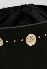 Sac en suède noir avec un dessus froncé, comportant deux ornements circulaires dorés et de petites clous dorés le long du côté.