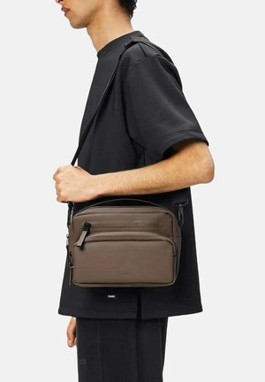 Borsa a tracolla marrone in materiale liscio, con diversi scomparti con zip, una tracolla nera e un sottile logo del marchio sulla parte anteriore.