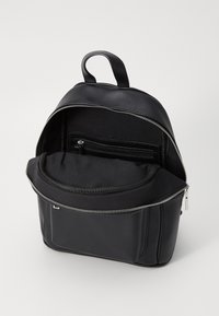 Zaino in finta pelle nera con chiusura a zip, tasche interne, una maniglia morbida e una forma strutturata. Presenta una texture liscia e un design minimalista.